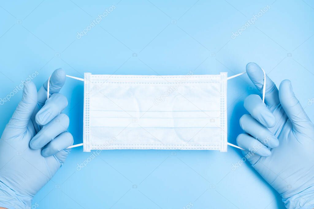 Hand gloves hold face mask in blue background