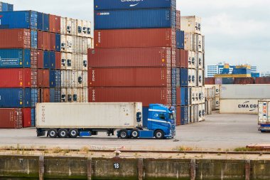 Rotterdam 'daki konteynır terminalinde konteynır yığını önünde kamyon var.