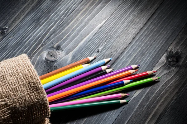 Colored pencils on black wooden table — Stock Photo, Image