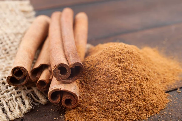 Paus de canela e pó de canela na placa de madeira marrom . — Fotografia de Stock