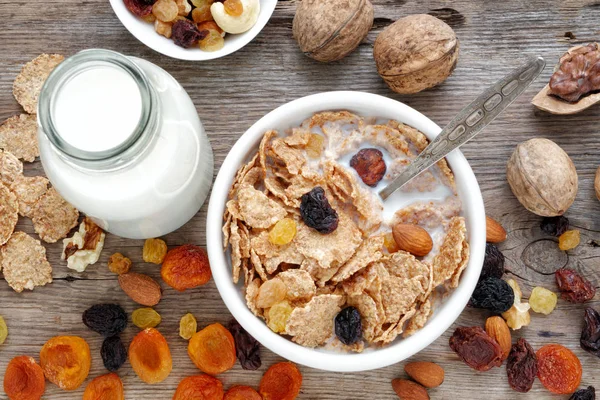 Desayuno saludable: cereales copos de trigo con leche en tazón, frutas secas en la mesa . —  Fotos de Stock