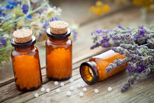 Bottles of homeopathic globules and healing herbs on wooden board. — Stock Photo, Image