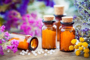 Bottles of homeopathic globules, mortar, healing herbs and flowers. clipart