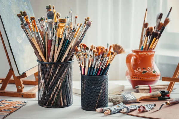 Attrezzature artistiche: cavalletto, pennelli, tubi di vernice, tavolozza e dipinti su tavolo da lavoro in studio d'artista . — Foto Stock
