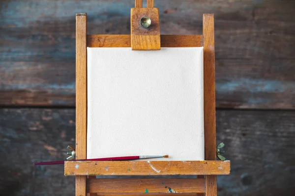 Empty canvas on easel on old wooden background. — Stock Photo, Image