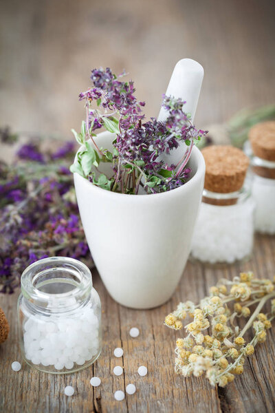 Mortar of dried healing herbs and bottles of homeopathic globules,