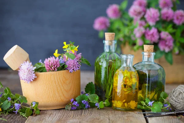 Bottles of tincture or infusion of healthy herbs, healing herbs and wooden mortar of flowers on rustic table. Herbal medicine. — Stock Photo, Image