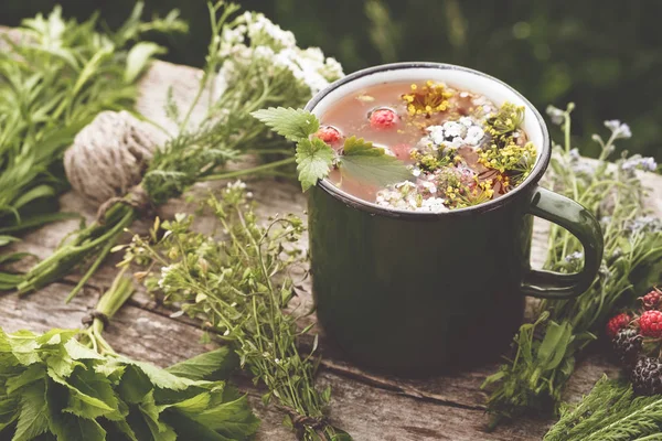 Letní zdravý bylinkový čaj ve staré smaltované hrnek a hrozny z léčivých bylin na dřevěné desce. Bylinné medicíny. Retro tónovaný fotografie. — Stock fotografie