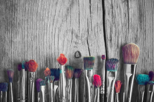 Row of artist paintbrushes with colorful bristle closeup on old wooden background, retro black and white stylized. — Stock Photo, Image