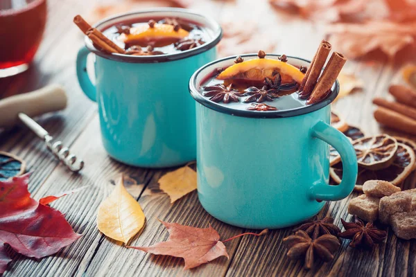 Glühwein in blau emaillierten Bechern mit Gewürzen und Zitrusfrüchten auf einem Holztisch mit Herbstblättern. Retro getönt — Stockfoto