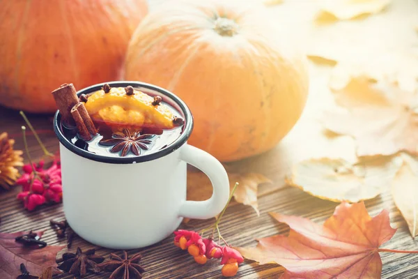 Vino rimuginato in tazza smaltata e zucche su tavolo in legno con foglie autunnali . — Foto Stock