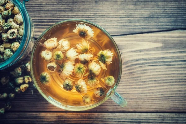 Taza de té de manzanilla saludable y frasco de vidrio de flores secas de margarita . —  Fotos de Stock