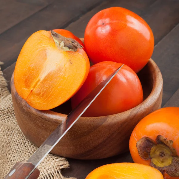 Persimmons in bowl with kitchen knife on wooden table. — Stock Photo, Image