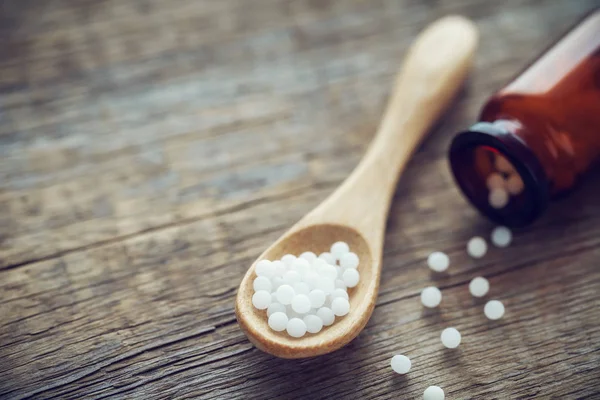 Houten lepel van homeopathische bolletjes, fles en verspreide korrels. Homeopathie geneeskunde. — Stockfoto