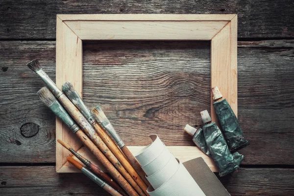 Wooden stretcher bar, paintbrushes, roll of artist canvas and paint tubes on old wooden background. Top view. Copy space for text. — Stock Photo, Image