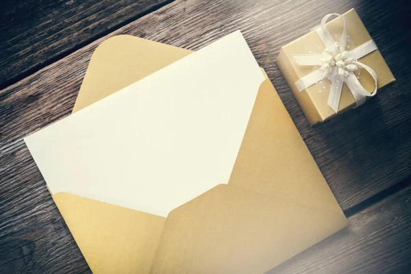 Offener gelber Papierumschlag mit leerem Papierblatt und Geschenkbox mit Schleife auf Holzplatte. — Stockfoto