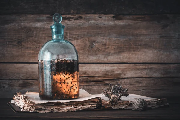 Tincture or potion bottle, old book and bunch of dry healthy herbs. Herbal medicine. Retro styled. — Stock Photo, Image