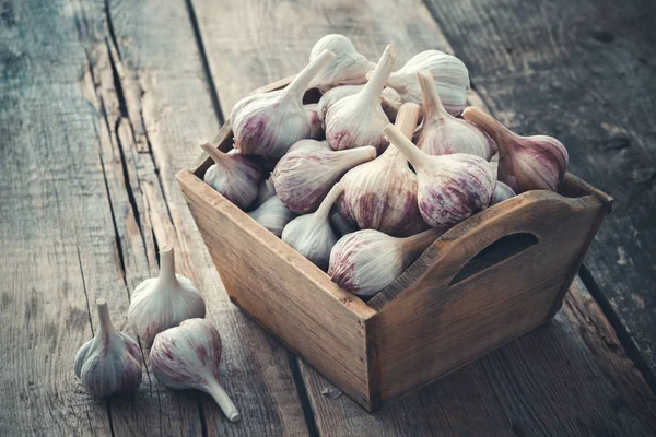 A lot of garlic in wooden box on wooden board. — Stock Photo, Image