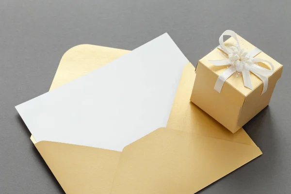 Offener gelber Papierumschlag mit leerem Blatt Papier und Geschenkschachtel mit Band auf grauem Hintergrund. — Stockfoto