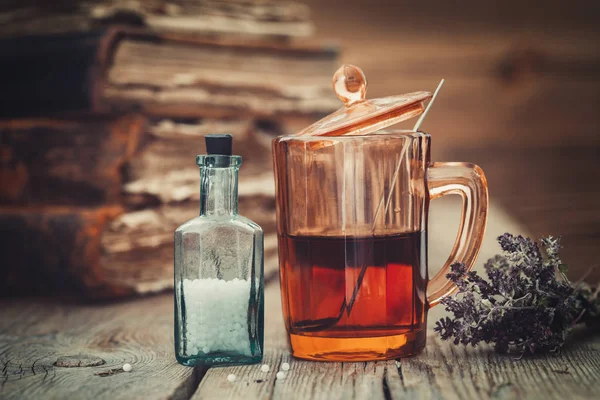 Настойка или здоровый чай в стакане, флакон гомеопатических глобул, старые книги и куча сухих здоровых трав . — стоковое фото