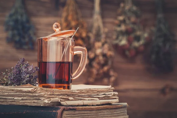 Taza de té saludable o tintura de hierbas en la pila de libros antiguos. Manojos colgantes de hierbas medicinales . — Foto de Stock