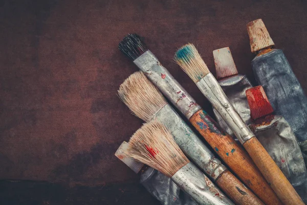 Artist paintbrushes, paint tubes closeup on brown canvas background. Copy space for text. — Stock Photo, Image