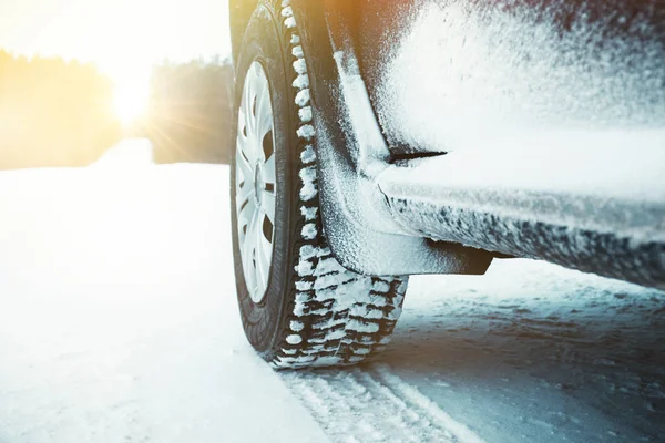 Pneus de carro cobertos de neve na estrada de inverno através da floresta no dia ensolarado . — Fotografia de Stock