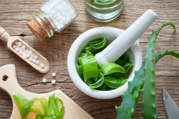 Frische Aloe-Vera-Blätter, Mörser voller gehackter Aloe und eine Flasche homöopathischer Globuli. Ansicht von oben. — Stockfoto