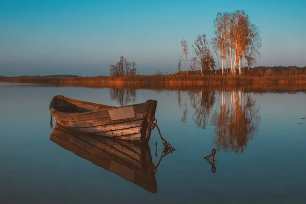 Fa evezős csónak tükröződik egy csendes tó víz alkonyatkor őszi táj. — Stock Fotó
