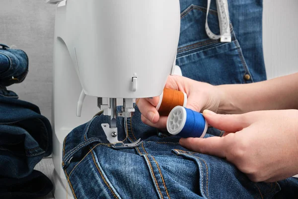 Costura vaqueros en la máquina de coser en taller de sastrería. La mujer elige el color de los hilos de coser de dos bobinas . — Foto de Stock