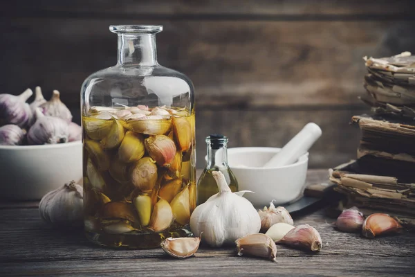 Garlic aromatic flavored oil or infusion bottle and garlic cloves. Mortar, old recipe books, kitchen knife. Garlic cooking. — Stock Image Garlic aromatic flavored oil or infusion bottle and garlic cloves. Mortar, old recipe books, kitchen knife. Garlic cooking. Stock Image