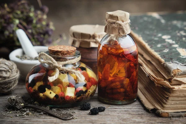 Bottles of essential oil or infusion, mortar and old book. Herbal medicine. — Stock Photo, Image