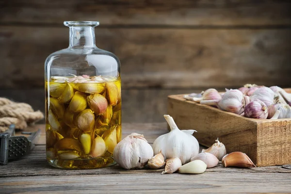 Garlic aromatic flavored oil or infusion bottle, wooden crate of garlic cloves and garlic press on kitchen table. — Stock Image Garlic aromatic flavored oil or infusion bottle, wooden crate of garlic cloves and garlic press on kitchen table. Stock Picture