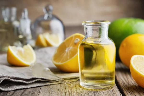 Butelka cytrynowego olejku eterycznego i owoców cytrusowych na stole. — Zdjęcie stockowe