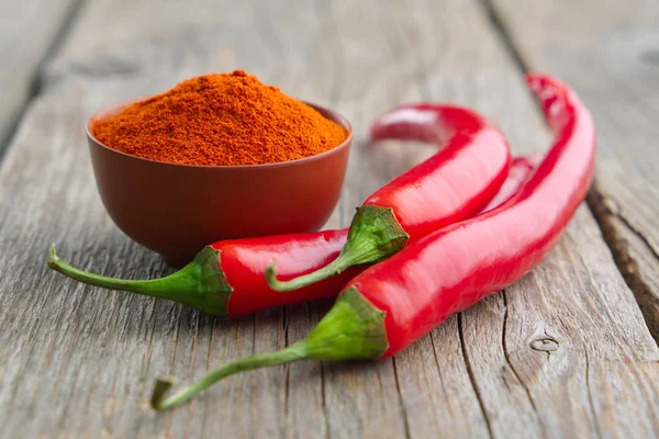 Whole and ground to powder red chili pepper on wooden kitchen table. — Stock Photo, Image