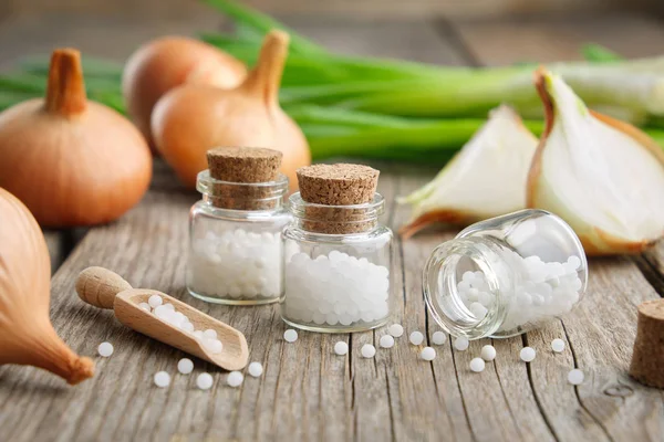 Onion bulbs, green onions and bottles of homeopathic globules. Allium cepa homeopathic remedies. — Stock Photo, Image
