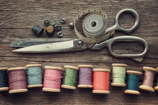 Rij van vintage houten spoelen van veelkleurige draden, maatschaar, vingerhoeden, meetlint, naaiwerk op houten plank. Uitzicht van bovenaf. — Stockfoto