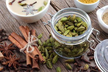 Bir kavanoz aromatik kakule kapsülü ve aromalı bir fincan sağlıklı ayurvedic masala çayı. Tarçın çubukları, kakule, karanfil ve anason yıldızları masada.. 
