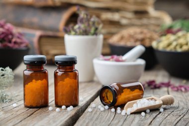 Arka planda homeopatik küreler, kitaplar, havanlar ve şifalı bitkiler var. Homeopati ilacı..