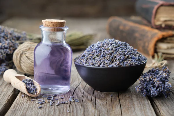Dry lavender flowers in bowl and bottle of essential lavender oil or infused water. Old books and lavender flowers bunch on background. 