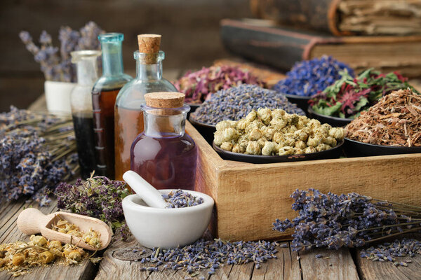 Bottles of healthy tincture or infusion, mortar and bowls of medicinal herbs in wooden crate, stack of old books on background. Herbal medicine.