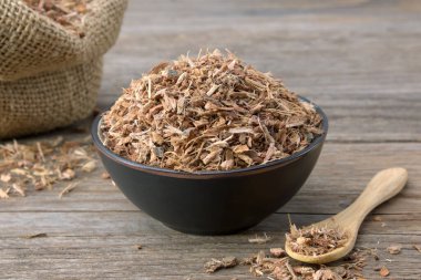 Siyah seramik kasede sağlıklı meşe kabuğu ve arka planda bir çuval kuru meşe kabuğu. Bitkisel ilaçlar.