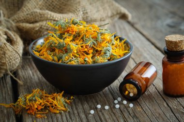 Homeopatik takvim granülleri, kasede sağlıklı kadife çiçekleri ve tahta masada çuval. Homeopati ilacı..