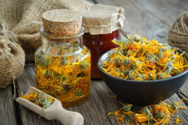 Bottles of calendula infusion or oil, healthy marigold flowers in bowl and calendula salve on wooden table. Herbal medicine. clipart