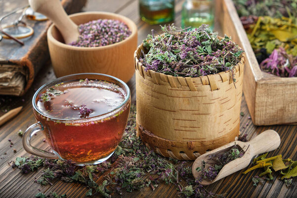 Cup of tea with wild Marjoram and Erica flowers. Dry Origanum vulgare and heather medicinal plants, old book and bottles of essential oil on background.