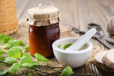 Bottle of birch herbal salve, balm or coal tar oil, healthy birch leaves, mortar on wooden table. Alternative medicine. clipart
