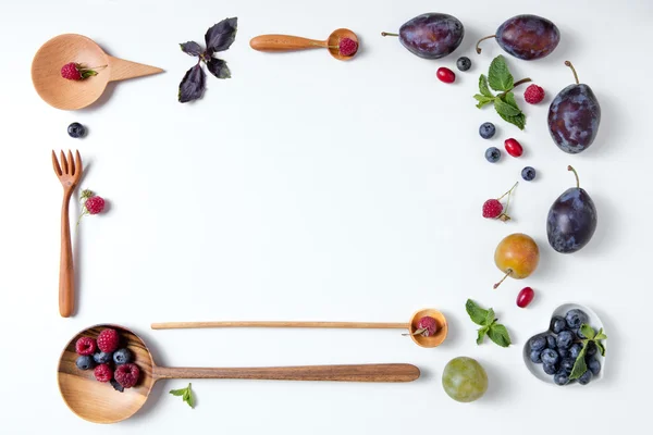 Frame of spoons with berries and plums — Stock Photo, Image