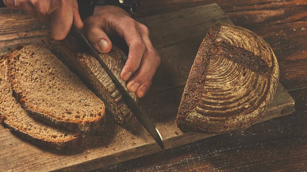 Male baker slicing dark bread — Stock Photo, Image