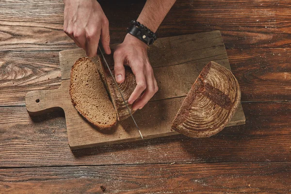 Человек режет хлеб из ржаного зерна — стоковое фото