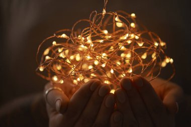Noel ışıkları elektrik çelenk koyu arka plan üzerinde tutan eller